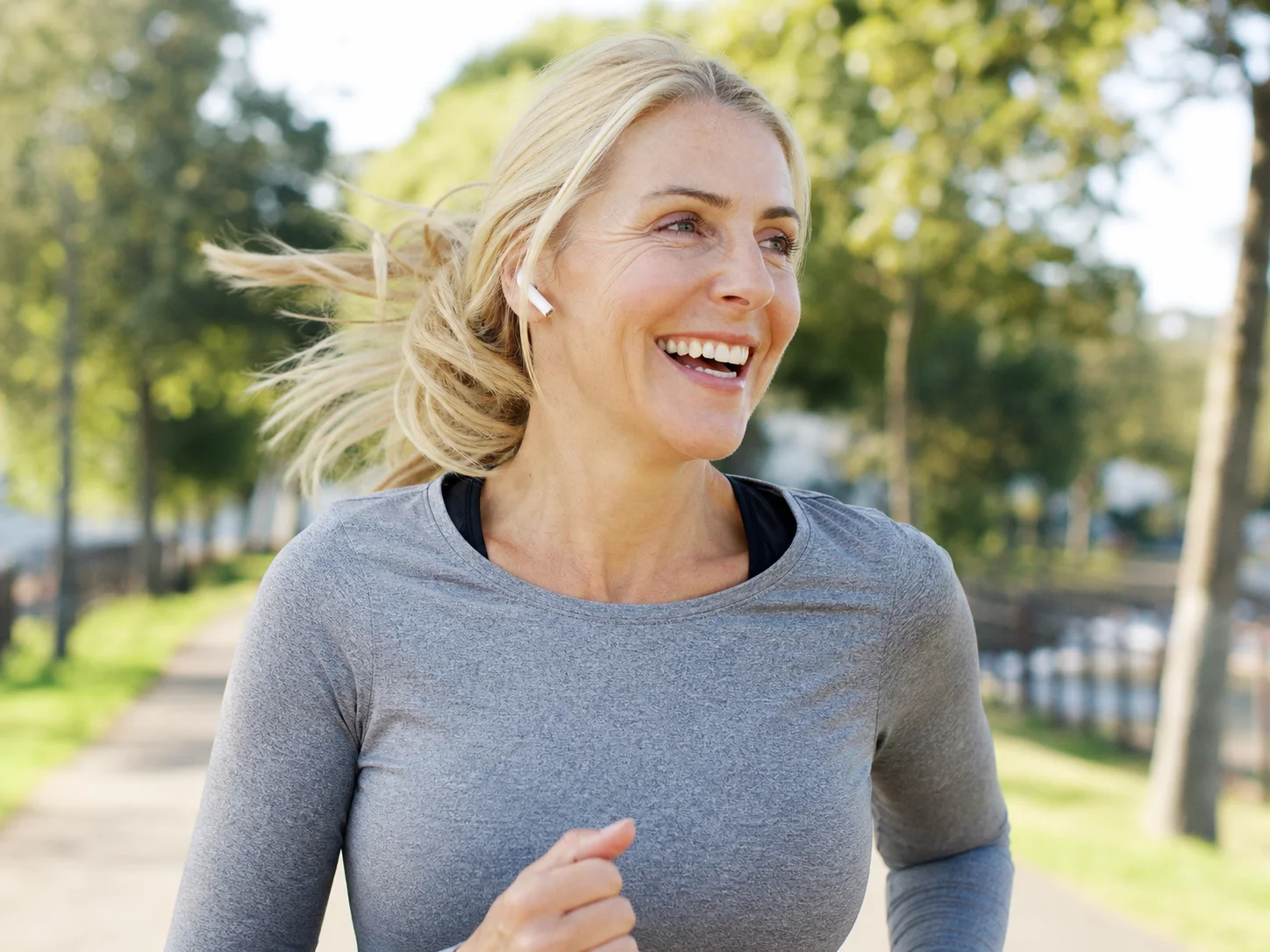 A blonde woman smiling during an ordinary morning jog through a neighborhood park